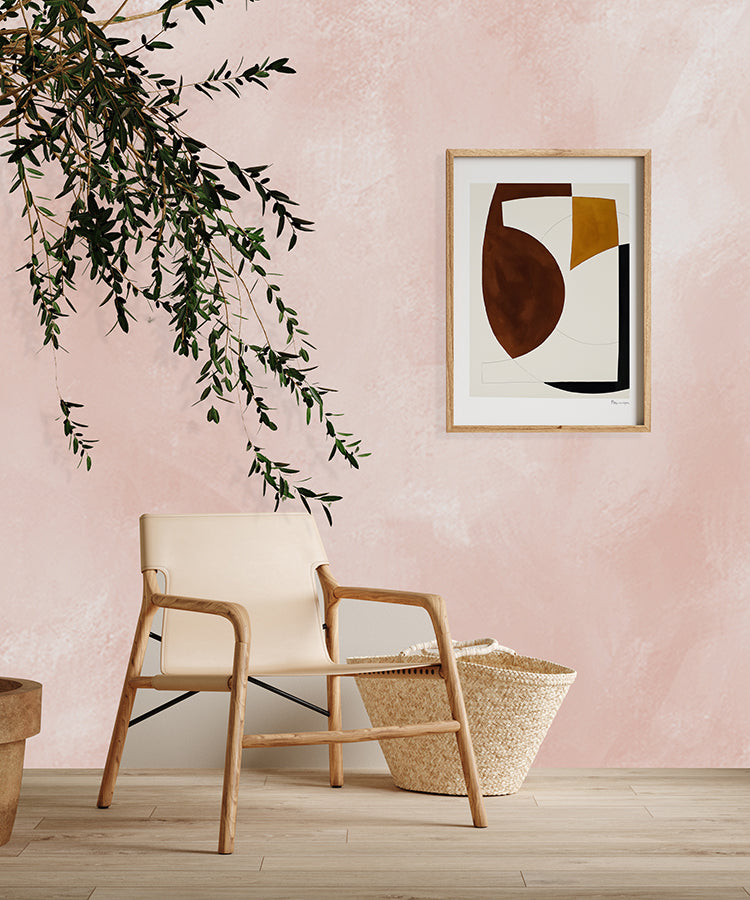 A contemporary room adorned with Addison Chalk, Ombre Wallpaper in Blush Pink, sets a tranquil mood. A modern beige armchair, a woven basket, and a framed abstract artwork add elegance. The room’s minimalist design, complemented by a touch of greenery, exudes a serene and inviting atmosphere.