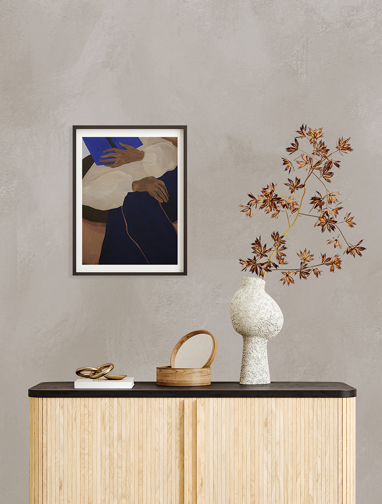 The room features Addison Chalk, Ombre Wallpaper in Sand. A wooden console table holds a framed abstract artwork, a reddish-leaved plant, and decorative objects. The overall ambiance is modern and stylish.