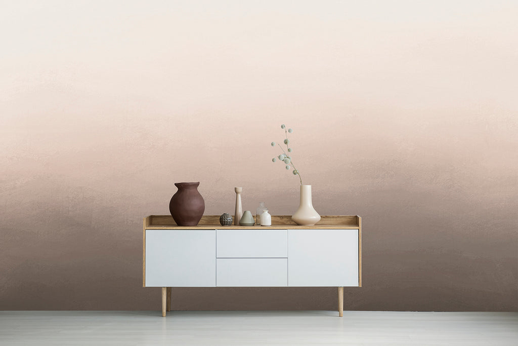 A minimalist room with a wooden console table against a wall featuring the Blake Horizon, Ombre Mural Wallpaper in Sand. Featuring various ceramic vases on a side board.