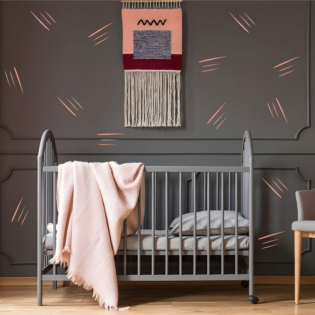 A cozy nursery room with gray crib and soft pink blanket, beside a matching gray armchair with cushion. Above, a woven wall hanging adds texture, set against the Boho Thin Lines, Wall Decals backdrop.