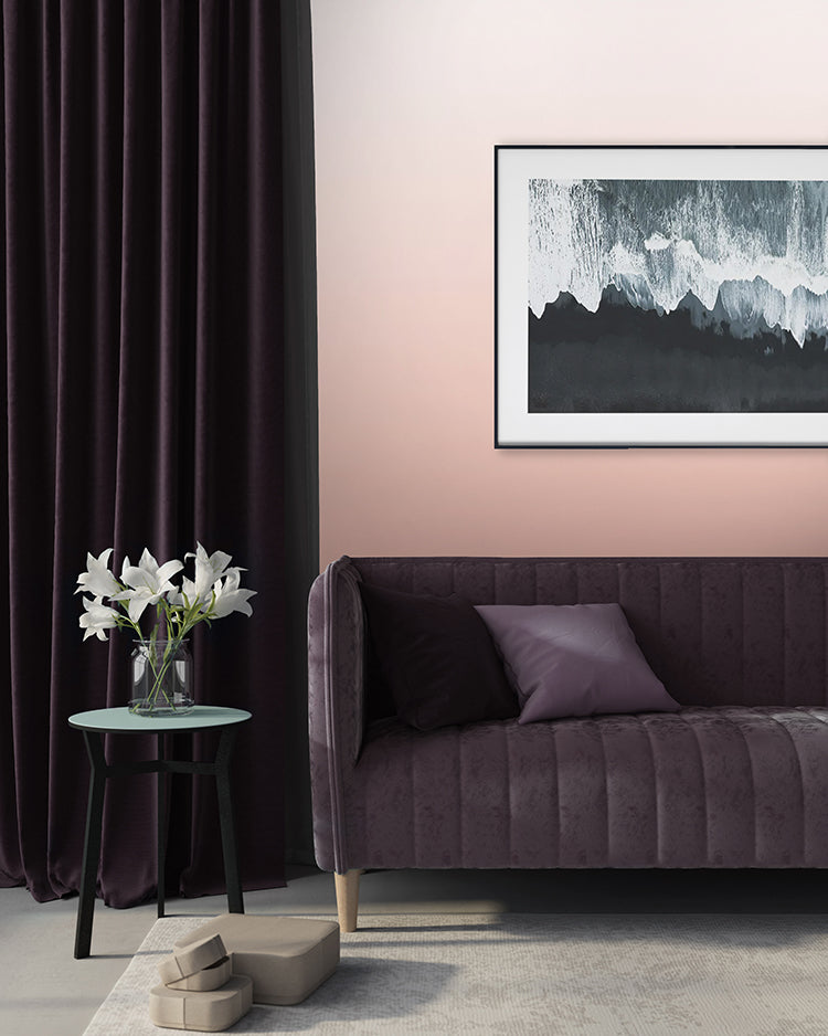 Modern room featuring Calbri Ombre Wallpaper, transitioning from Pink at the base to a lighter hue at the top. Complemented by a dark violet velvet sofa, a green round table with white lilies, and abstract art.