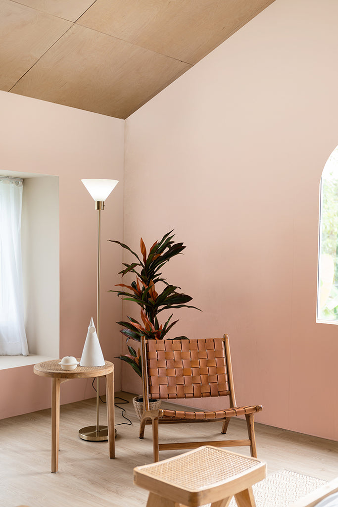 A serene room featuring a Calbri Ombre Wallpaper, a stylish leather chair, a round table with decor, an indoor plant, and a floor lamp near a window with sheer curtains.