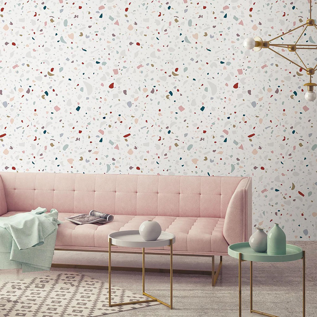 Stylish interior featuring Confetti Terrazzo, Pattern Wallpaper with multicolored speckles on a light background. Enhanced by a pink tufted sofa, modern tables, and chic decor for a trendy vibe.