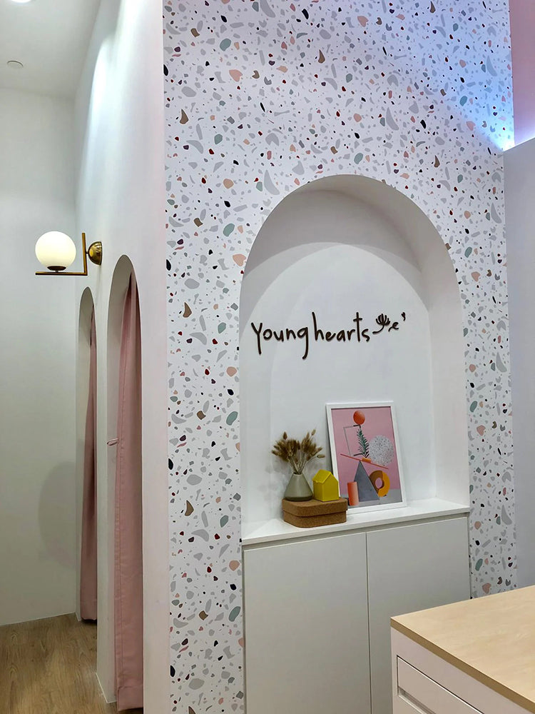 Vibrant and playful Confetti Terrazzo, Pattern Wallpaper enhancing a room’s decor, featuring an arched niche with the cursive text ‘Young hearts’, and a white cabinet adorned with decorative items and framed artwork.