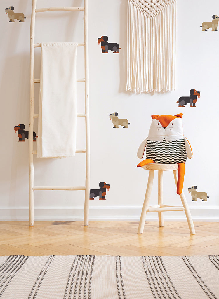 In a cozy children’s room, playful Doggies and Pups, Wall Decals adorn a white wall. The wooden ladder leans against the wall, draped with a soft cloth. An orange fox plush sits on a chair nearby, adding a touch of whimsy. A striped rug completes the charming decor.