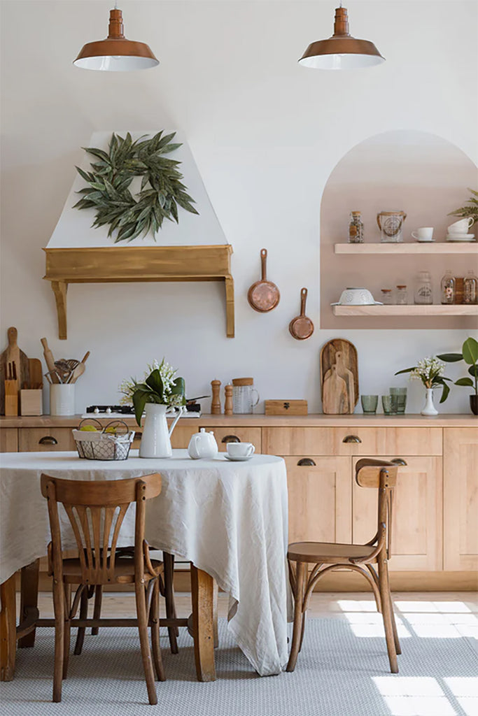 A rustic dining area with natural wood furniture, white walls, wooden utensils, potted plants, and pendant lights. Dome Ombre Gradient, Wall Decals in Nude subtly enhances the room’s charm.