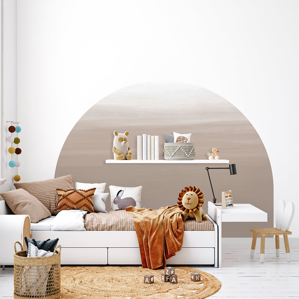 Earthy tones create a calming atmosphere in a minimalist children’s room features Dome Ombre Gradient, Wallpaper. A white daybed with lion-shaped pillows, a wooden stool, and a natural fiber rug complete the design. 