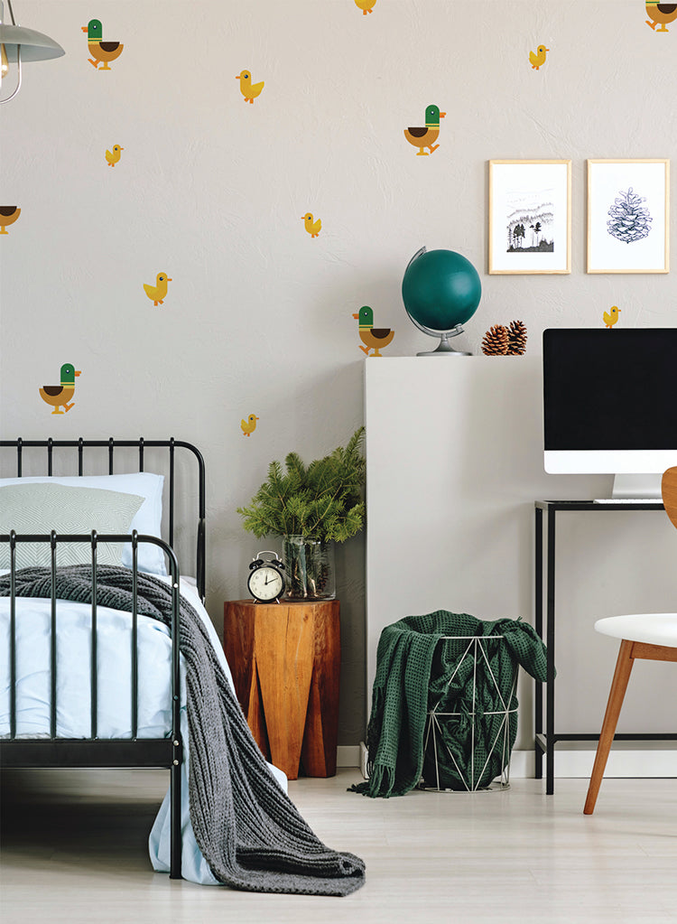 A cozy room with a black metal frame bed, white bedding, a wooden nightstand displaying a clock and a potted plant, and a desk with a computer. The walls are adorned with charming Duck and Ducklings, Wall Decals.