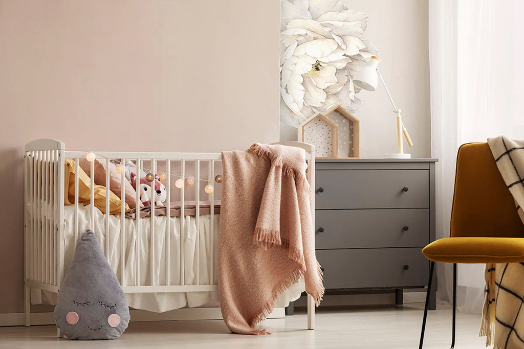 A serene nursery room with an Extra Large Solo Peony, Wall Decals in White. A white crib with a pink blanket, a grey dresser, and a plush toy create a calming ambiance, enhanced by soft natural light.