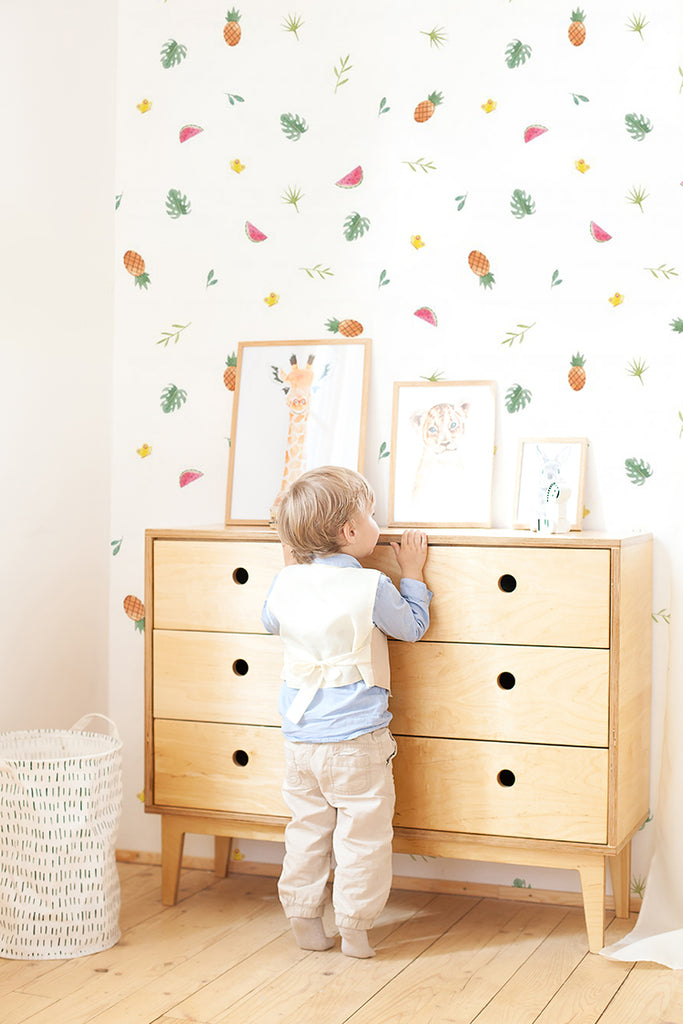 A lively room featuring Fruits Garden, Pattern Wallpaper, a vibrant pattern of assorted fruits and leaves. A curious child stands before a wooden dresser, engrossed in examining the framed artwork.