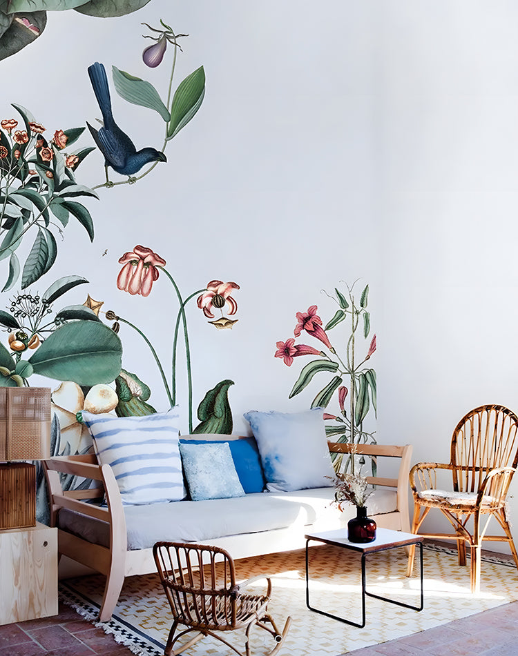 Bright room with large botanical prints of Garden Party, Mural Wallpaper. Wooden bench, rattan chairs, and a red vase complement the wallpaper.