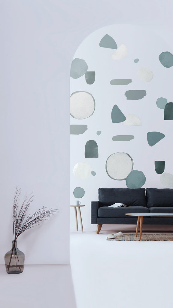 A modern room with minimalist design featuring a black sofa, wooden coffee table, and a tall vase with dried branches. The wall has abstract Glacier Colours, Wall Decals in cool tones.