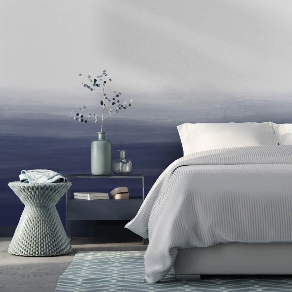 A tranquil bedroom featuring the Gradient Ombre, Mural Wallpaper Grey Blue. The wall displays a soothing transition from dark to light blue, complementing the room’s minimalist decor and white bedding.