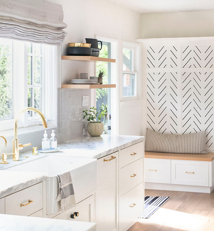Stylish kitchen featuring Herringbone Strokes, Pattern Wallpaper on the accent wall, complemented by white cabinets, gold fixtures, a cozy window seat, and chic floating shelves. Perfect for modern home decor inspiration.