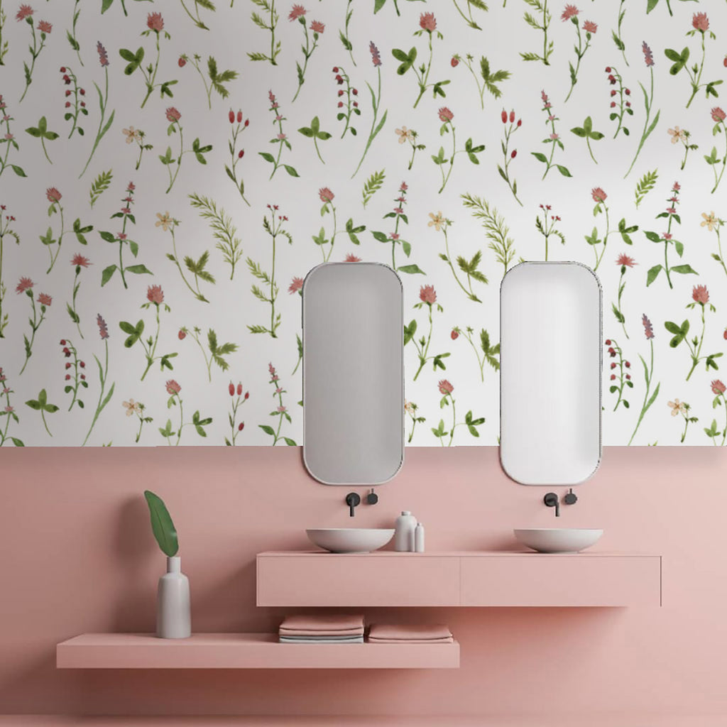 An image of a bathroom with a floral patterned wallpaper named Lila, Floral Pattern Wallpaper. The wallpaper features a variety of flowers and leaves. Two vertical mirrors hang above a pink shelf with two sinks, toiletries, and stacked pink towels.