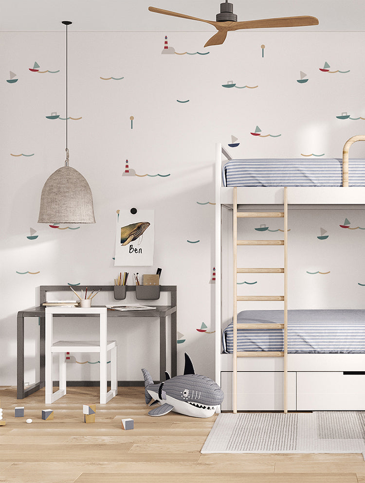A cozy child’s bedroom adorned with ‘Little Sailors’ pattern wallpaper in Blue Sand. The room features a sturdy bunk bed, a practical desk with a chair for studying, a ceiling fan for comfort, and a collection of plush toys adding a touch of playfulness.