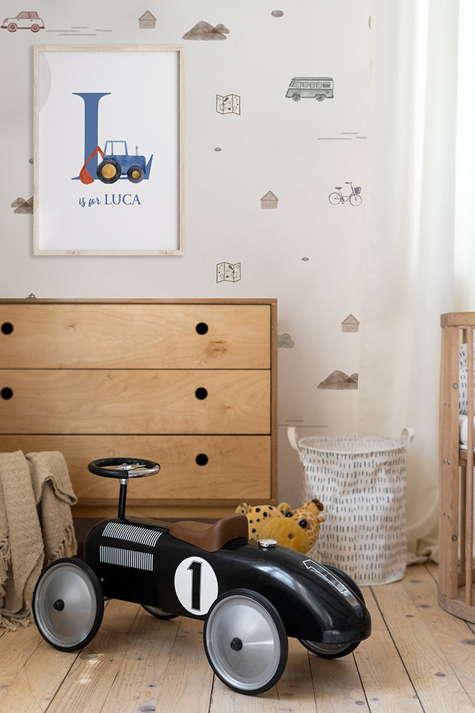 A vintage-inspired black toy car is the focal point of a nursery featuring the Mini Roadtrippers, Pattern Wallpaper in Grey. The wallpaper's subtle design complements the warm wooden furniture, including a dresser and crib. A personalized framed print adds a unique touch to the room.