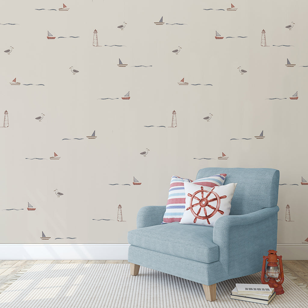 A cozy corner with Mini Seafarer, Pattern Wallpaper in Nude, featuring sailboats, lighthouses, and seagulls. A comfortable blue armchair with a nautical cushion is placed next to a small, charming red lantern.