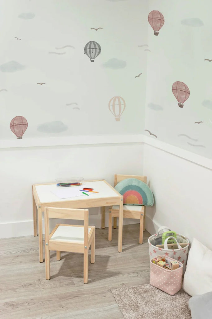 A vibrant children’s room adorned with ‘Mini Whimsical Air, Pattern Wallpaper in Blue, featuring whimsical hot air balloons and fluffy clouds. A cozy corner with a small wooden table, coloring materials, and a rainbow cushion, with a basket of toys on a rug.
