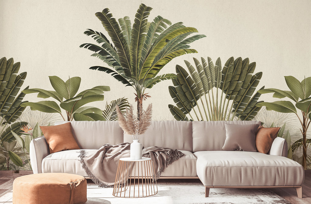 An elegant interior featuring a beige sofa with orange pillows, a small round table, and a tan ottoman. The Palm Paradise, Tropical Mural Wallpaper in Honey, adorned with green palm leaves, adds a vibrant, exotic touch to the stylish decor.