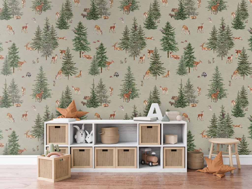 Pine forest, Pattern Wallpaper in green colourway, the room includes a white storage unit with woven baskets, a star-shaped cushion, a letter 'A,' and some books. Additionally, there is a wooden stool with another star-shaped cushion and a basket of toys on the floor. The room has a cozy wooden floor.