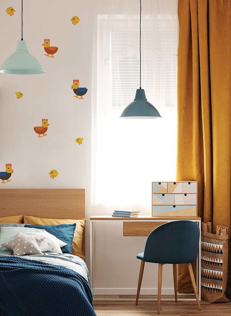A wooden bed with blue bedding sits in a sunlit room. Mustard curtains frame a bright window, and playful Rooster and Hen Family, Wall Decals featuring roosters, hens, and chicks adorn the walls