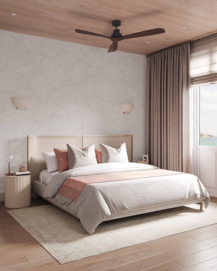 Serene bedroom with Saltwater Blooms, Pattern Wallpaper in Sand. Features include a cozy double bed, wooden side tables, wall-mounted lamps, a ceiling fan, and a window with sheer curtains. The room exudes a warm, inviting atmosphere.