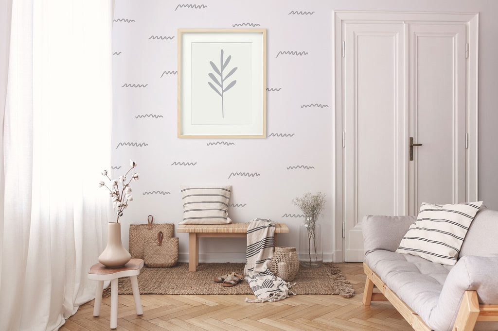 A serene room with a cozy ambiance, featuring a soft-hued sofa adorned with striped cushions, a wooden stool with a plant vase, and a bench with a woven bag beside it. A framed botanical print hangs on the wall with Scribbly Notes, Wall Decals.