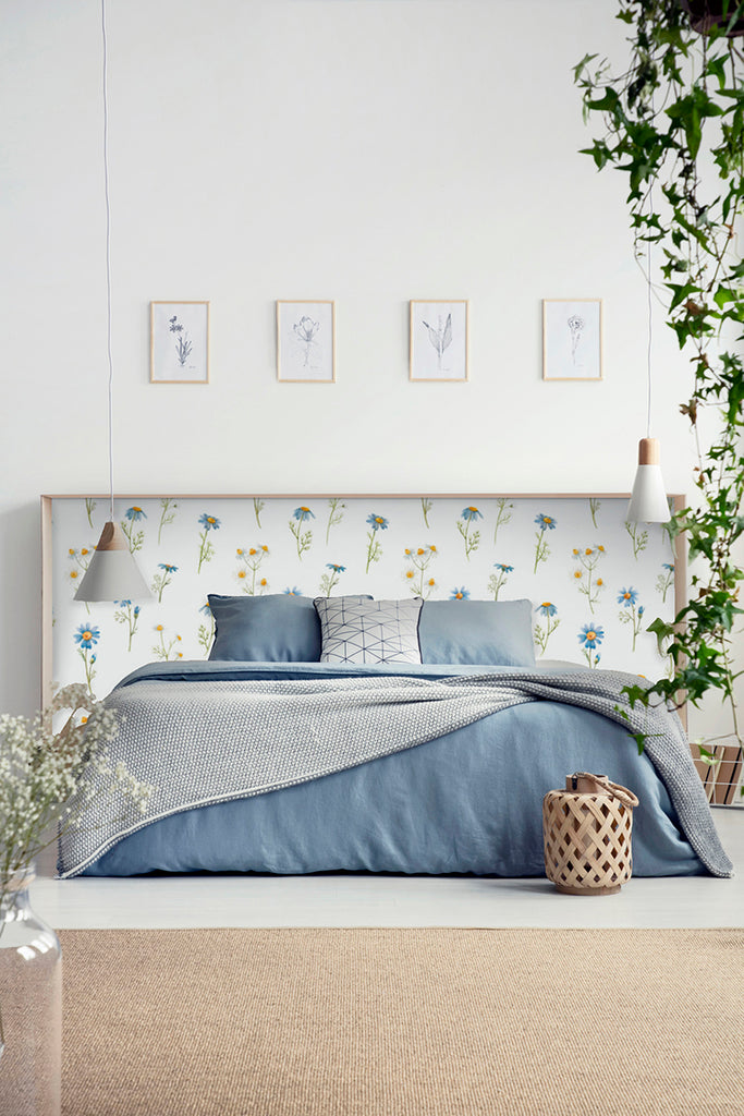 Sharon Floral Wallpaper adorning a bedroom wall, featuring a tranquil design of delicate flowers and birds. The room is furnished with a bed dressed in blue bedding, creating a serene and nature-inspired atmosphere.