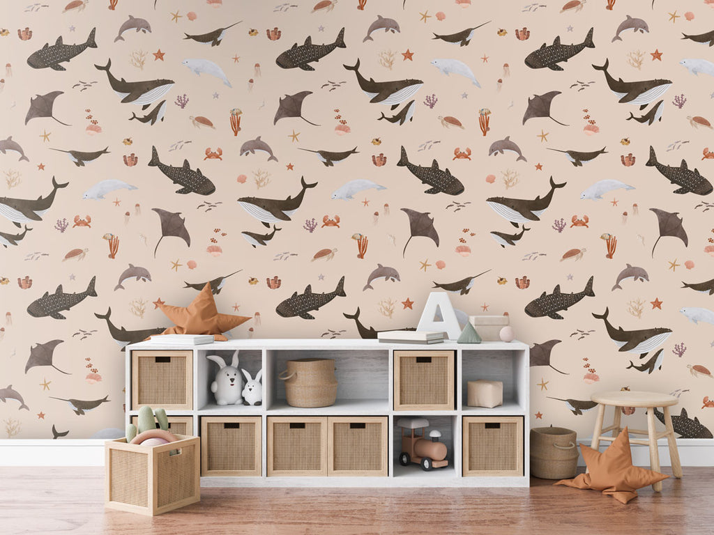 A children’s room with beige Splendid Sea wallpaper featuring whales, dolphins, and corals, and a storage unit with baskets.