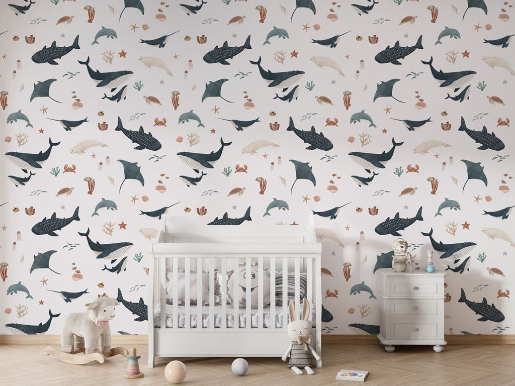 Minimal nursery with Splendid Sea white wallpaper showcasing whales, dolphins, and coral around a white crib.