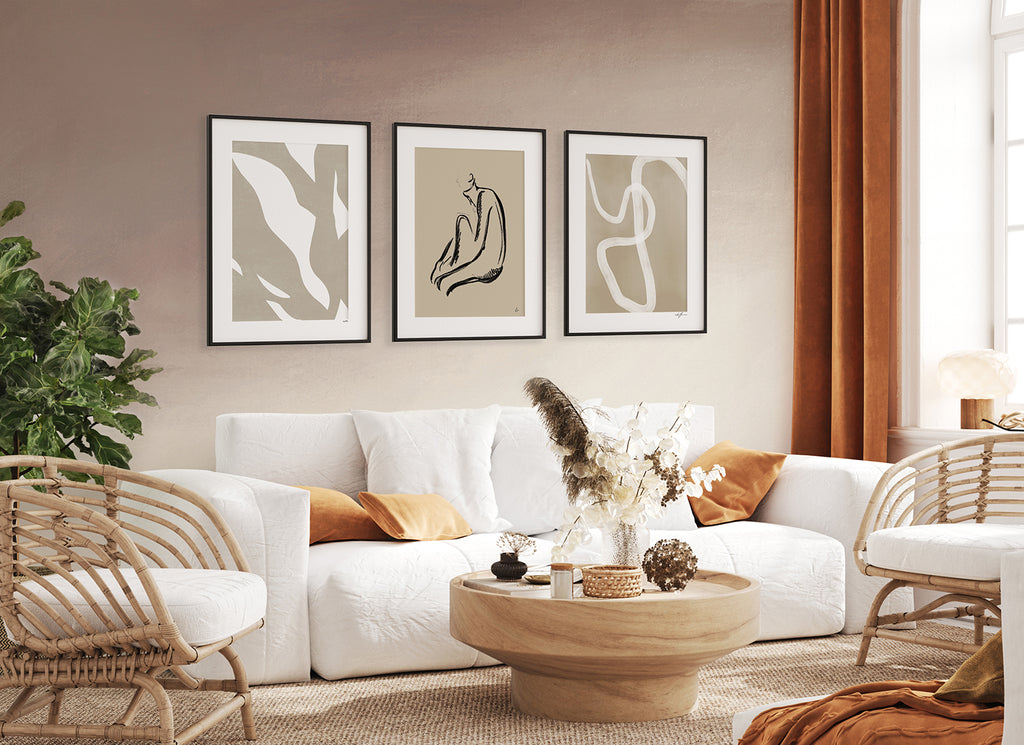 Cozy living room with a large white sofa, accented by vibrant orange pillows. Framed abstract art pieces on a wall with Stella Skies Ombre Wallpaper in Blush Pink add depth and modern aesthetics to the space.