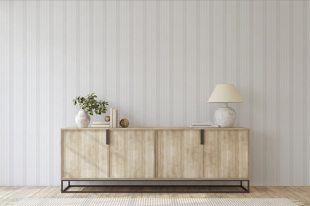 Minimalist room featuring Stripes Linen, Pattern Wallpaper in Light Grey, a wooden sideboard with a lamp, a plant in a vase, and decorative items, creating a modern and elegant space.