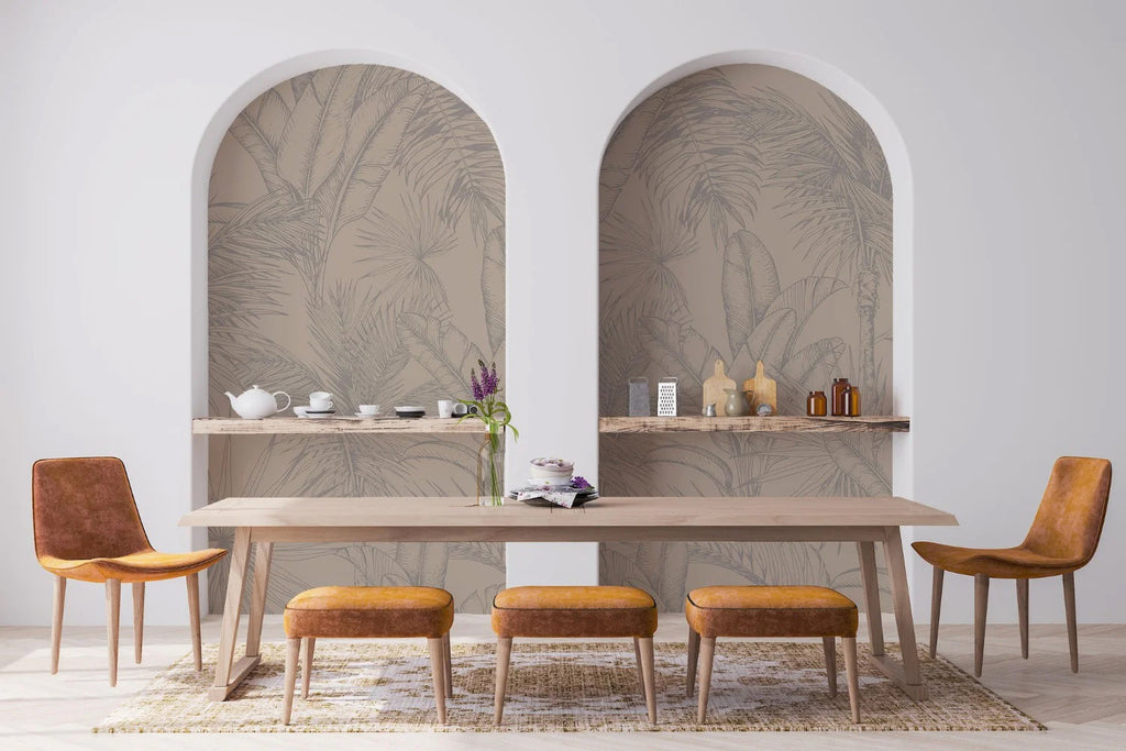 A room with Tropics Botanical, Mural Wallpaper in Sand, featuring large palm leaf patterns in muted tones. Centered is a wooden table with matching chairs and decorative items.