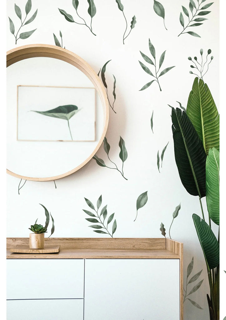 Serene room adorned with Watercolour Foliage by Megan pattern wallpaper. A modern white dresser under a round wooden mirror, and a small potted plant, enhance the room’s fresh, botanical ambiance.