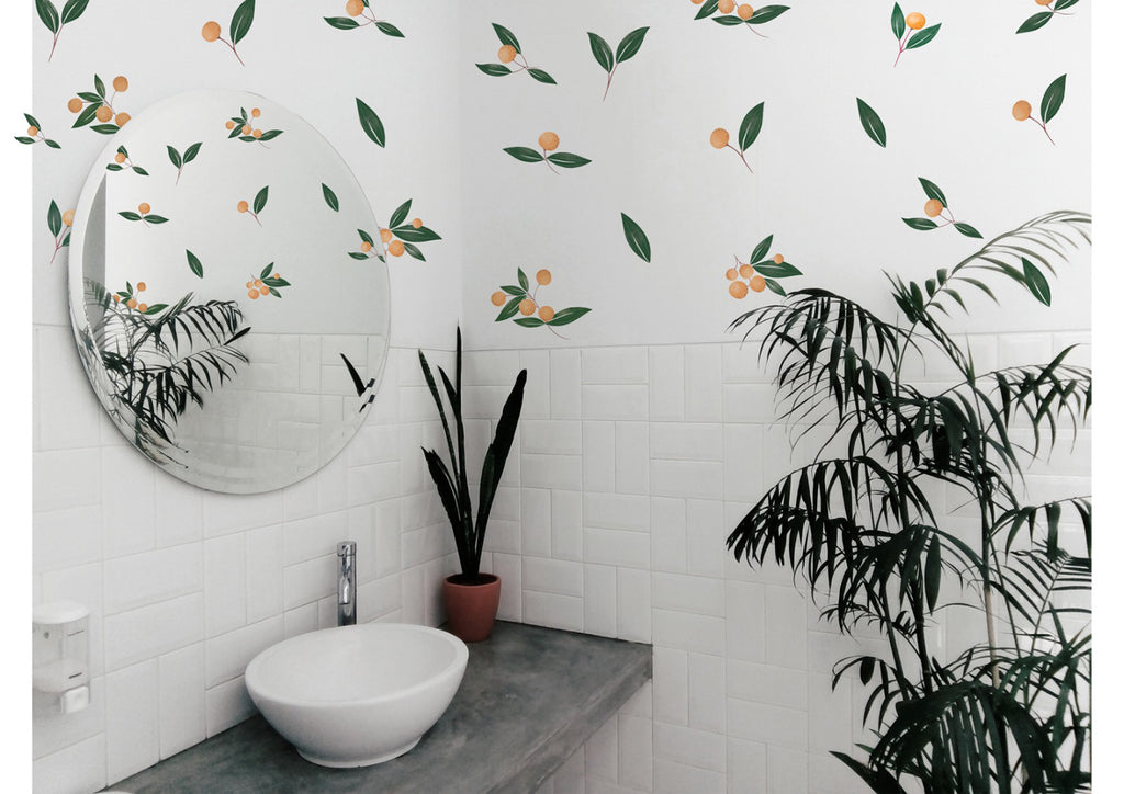 A modern bathroom with a white vessel sink, gray countertop, and large round mirror. Lush green potted plants add vibrancy against white subway-tiled walls adorned with Watercolour Oranges, Wall Decals decals.