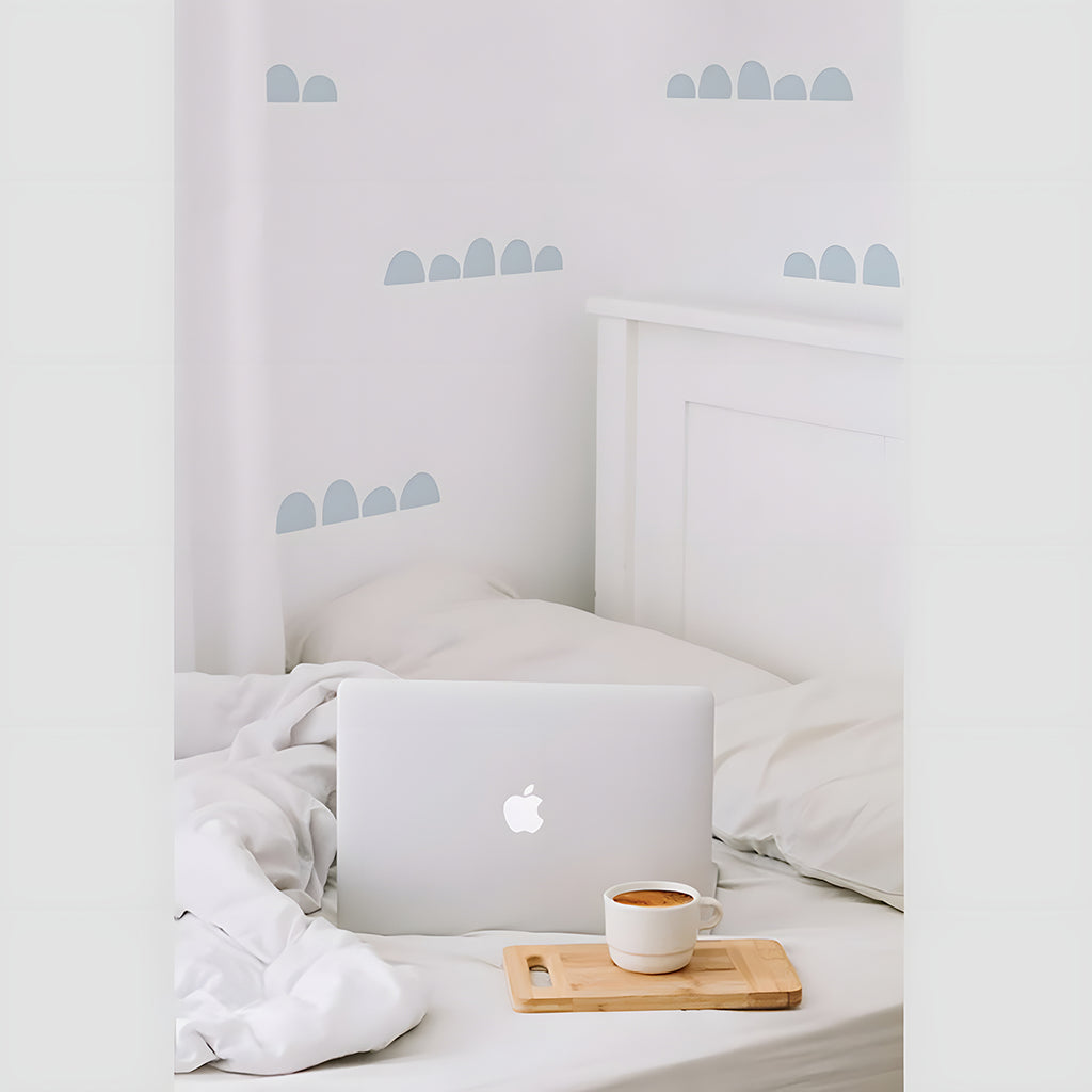 Serene bedroom with white bed, rumpled sheets, wooden bedside tray, laptop, and cup against a soft-hued wall with Wide Spaced Scallops, Wall Decals .