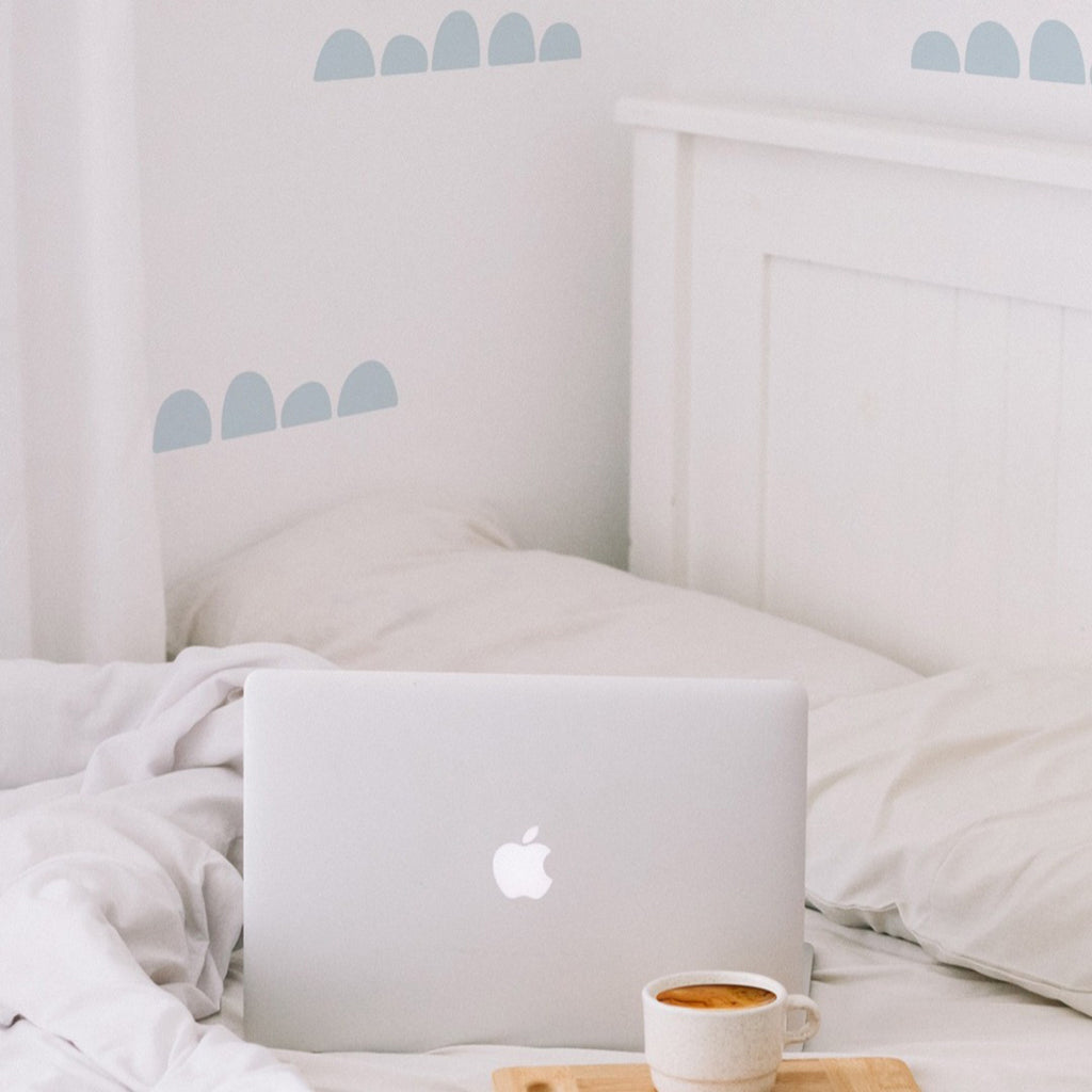 Serene bedroom with white bed, rumpled sheets, wooden bedside tray, laptop, and cup against a soft-hued wall with Wide Spaced Scallops, Wall Decals .