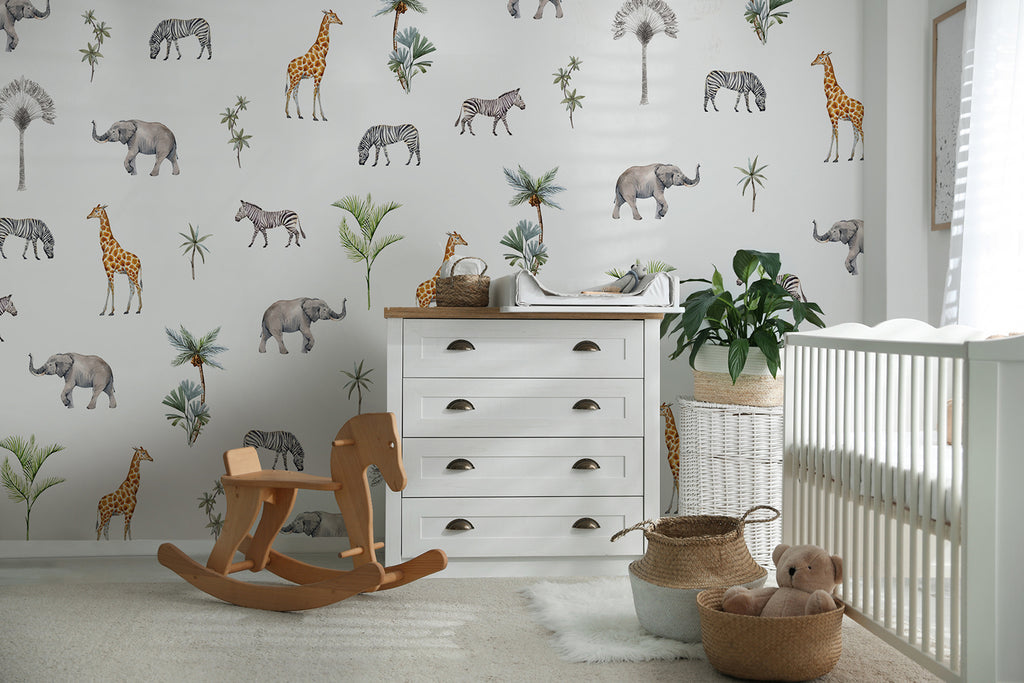 A serene nursery room adorned with Woodland Animals, Pattern Wallpaper in Multicolor, showcasing elephants and zebras amidst foliage. A white crib, rocking horse, and other nursery essentials complement the whimsical decor.