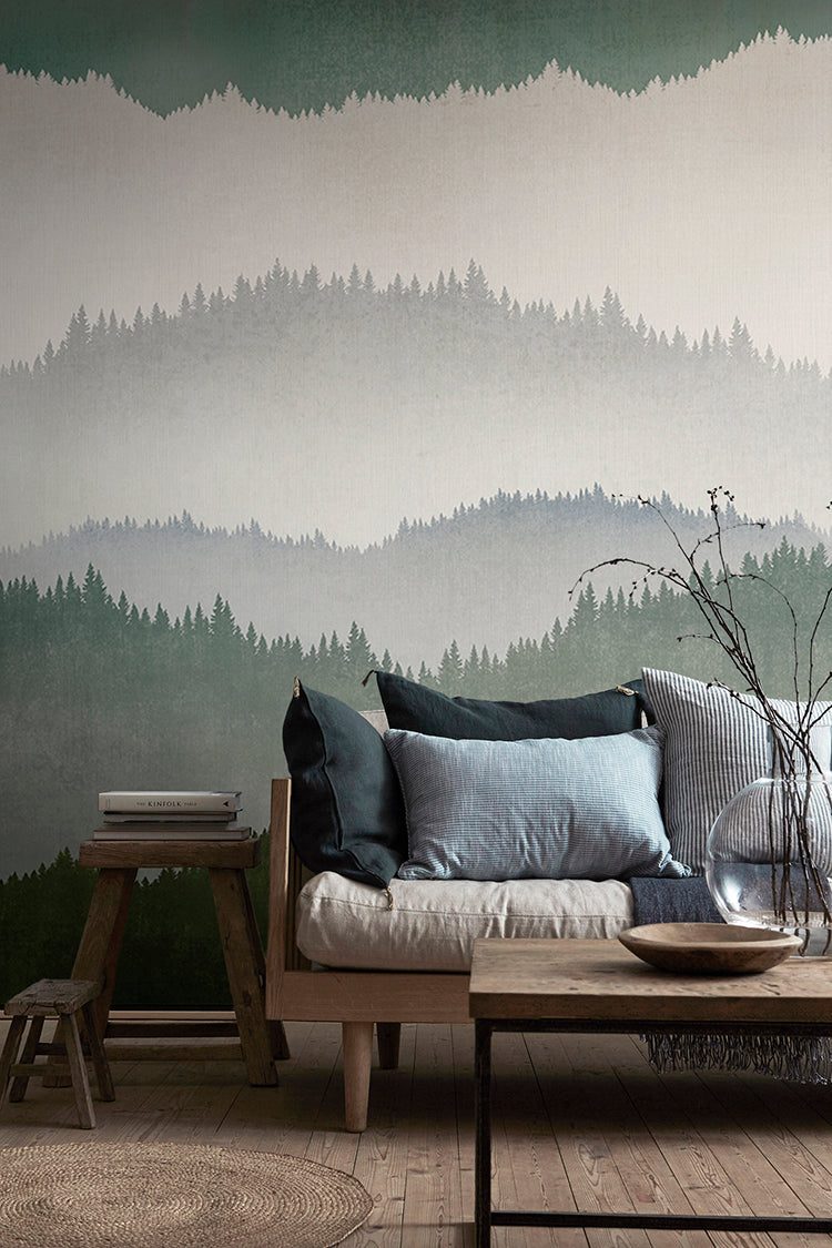 Forest Landscape, Ombre Mural Wallpaper in Dark Green featured in a wall of a living area with wooden furnitures and flooring, with an assortment of pillows on top of a cushion.