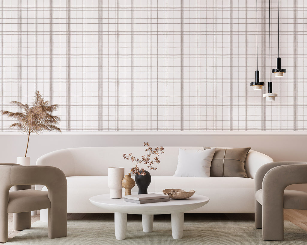 A modern living room featuring a white sofa with a grey cushion, a round table with decorative vases and a book, all set against a backdrop of Hand-Drawn Plaids, Pattern Wallpaper in Brown