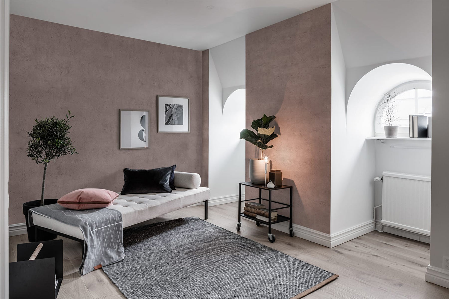 Blush Solid, Concrete Wallpaper featured on a wall of a living area with white sofa and grey throwover. Along with a light brown flooring