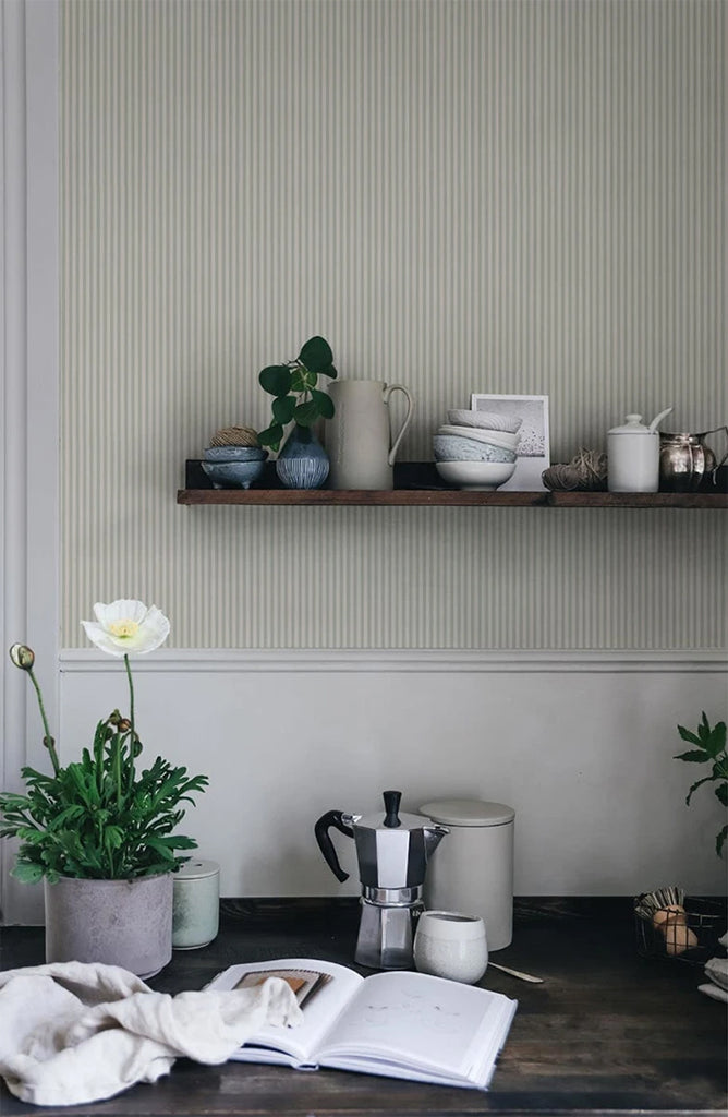 Laura Stripes, Pattern Wallpaper in sage featured on a wall of a room with a wooden table with books and furniture
