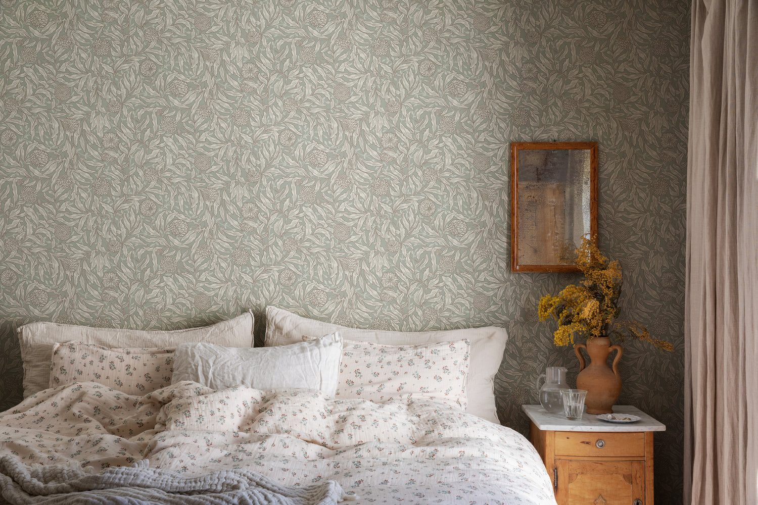 Olof, Floral Pattern Wallpaper in Green  featured on a wall of a bedroom with a bed with a wooden side table with flower on it.