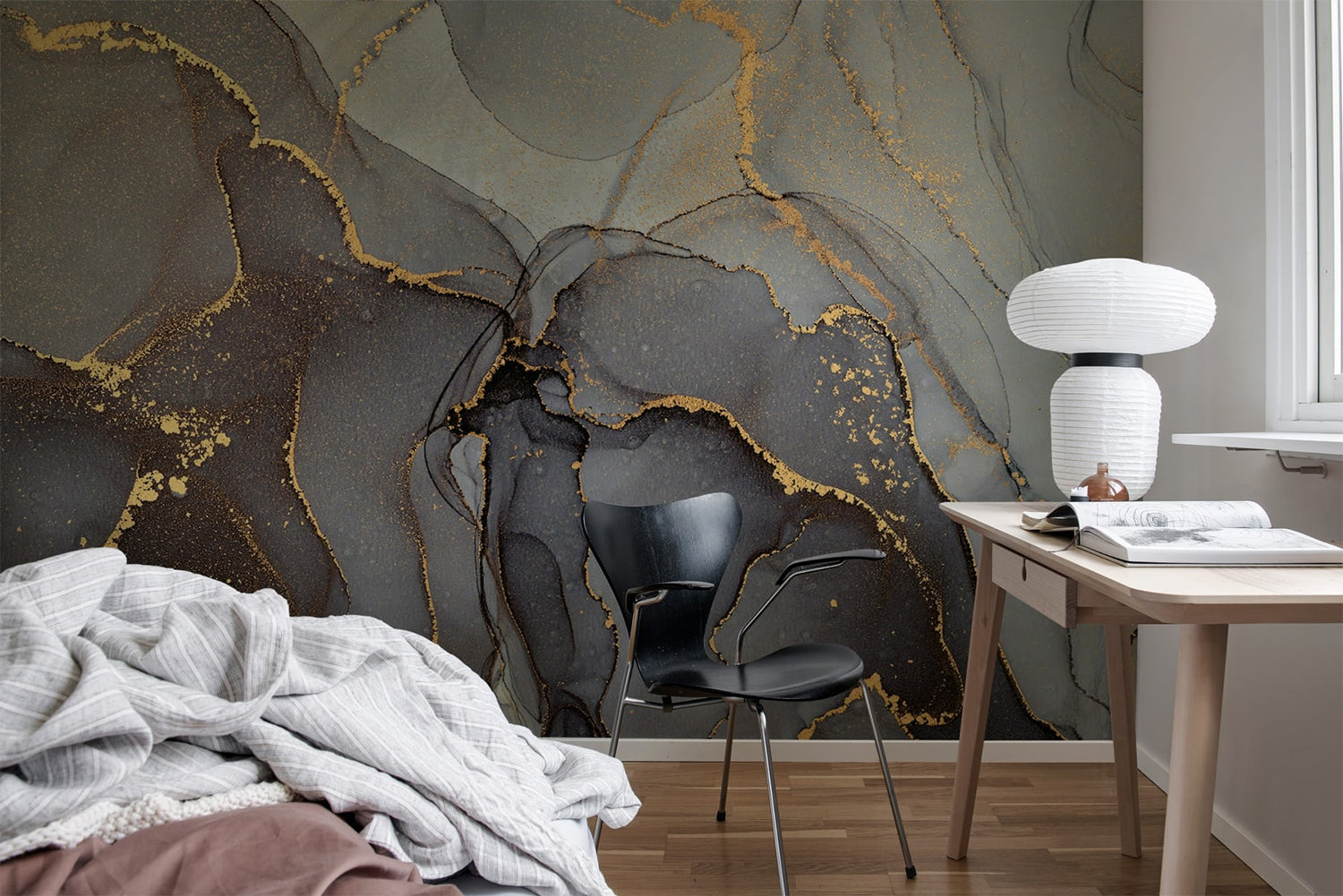 Agate Crystal Marble Texture Wallpaper in Onyx Black featured on a wall of a bedroom with a part of the bed seen, along with a wooden study table that has a book and a lamp, and a black chair.