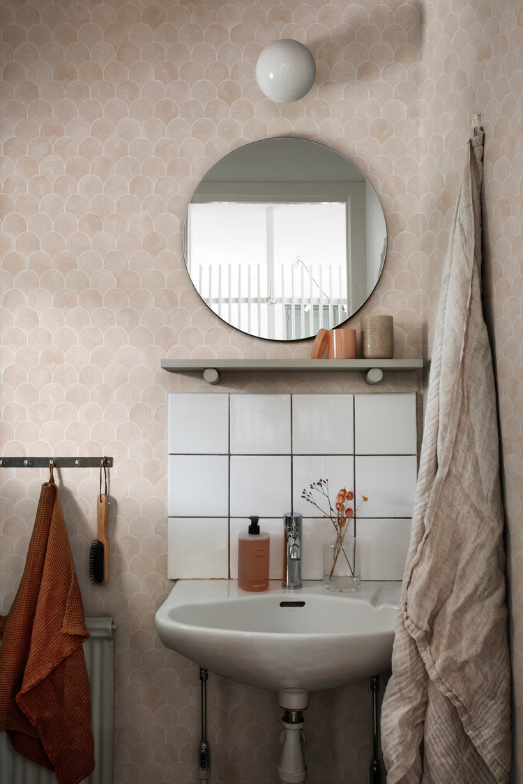 Igor Shells, Pattern Wallpaper in nude featured on a wall of a bathroom with a round mirror and a circular wall lamp