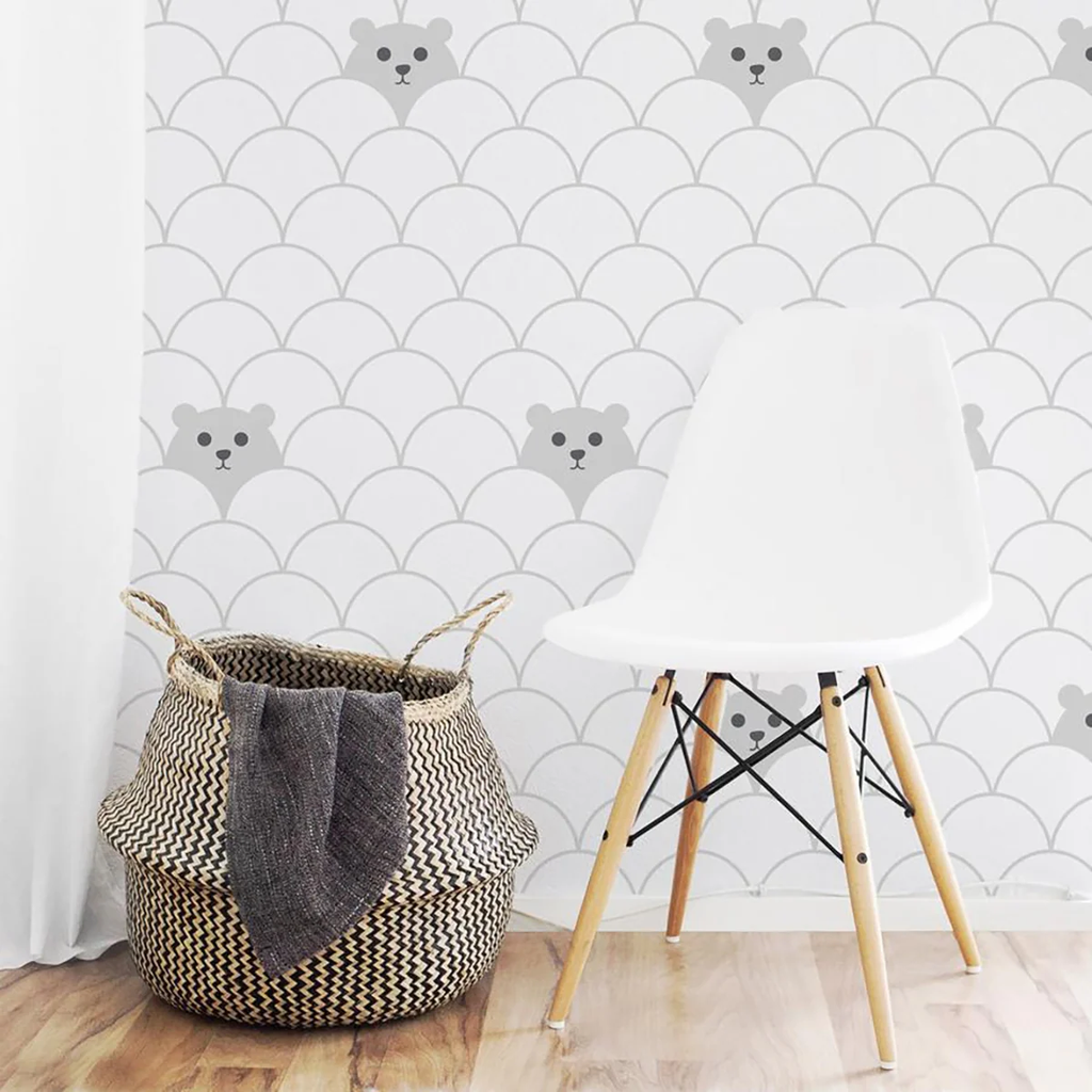 A playful room featuring Hide and Seek Bear, Pattern Wallpaper on a white backdrop. A modern white chair and a woven basket with a grey blanket are in front of the wallpaper. The floor is light-colored wood.
