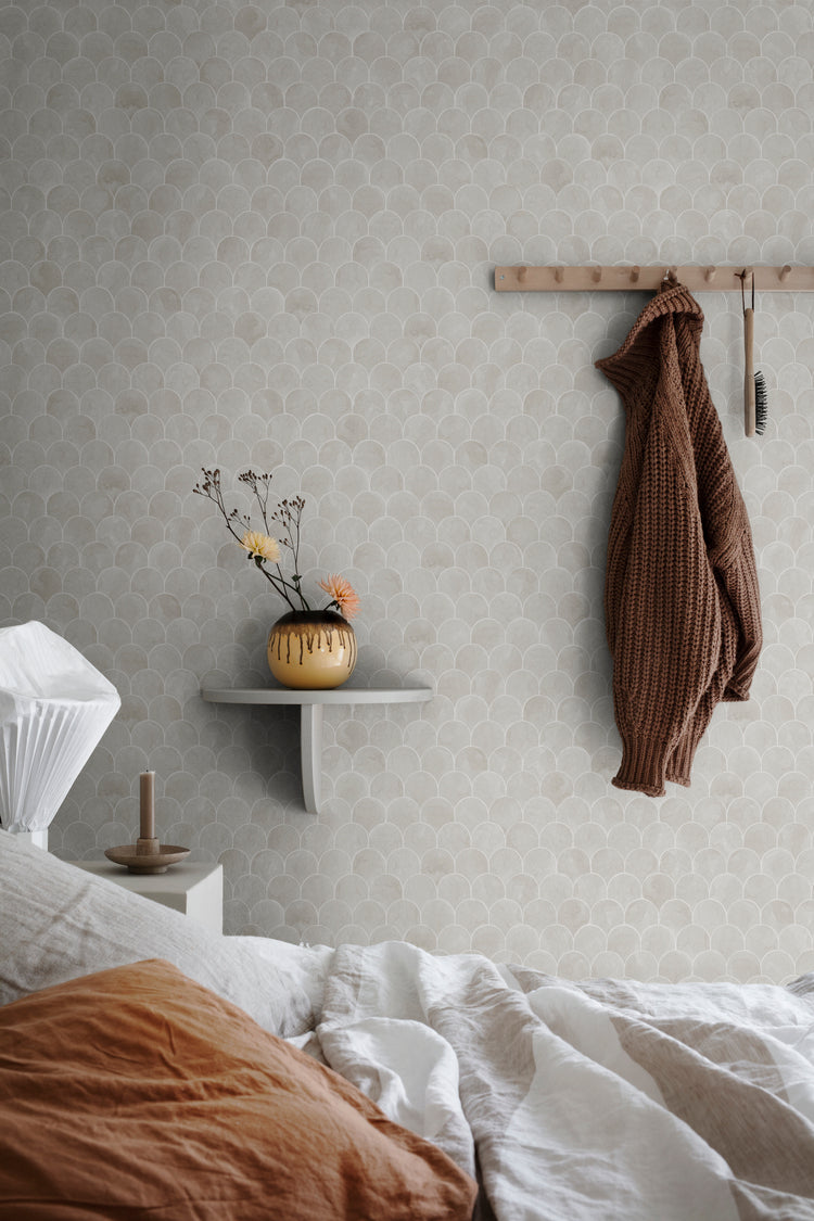 Igor Shells, Pattern Wallpaper in light grey featured on a wall of a bedroom with a comfy bed with white sheets and brown pillow and a cloth hanging on the wall