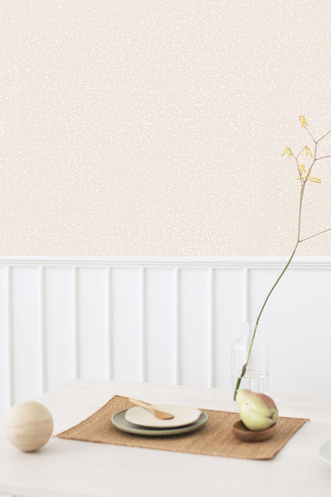 The dining room features a wall adorned with a speckle-patterned wallpaper in blush pink, and the table is set with an array of fruits and dishes.