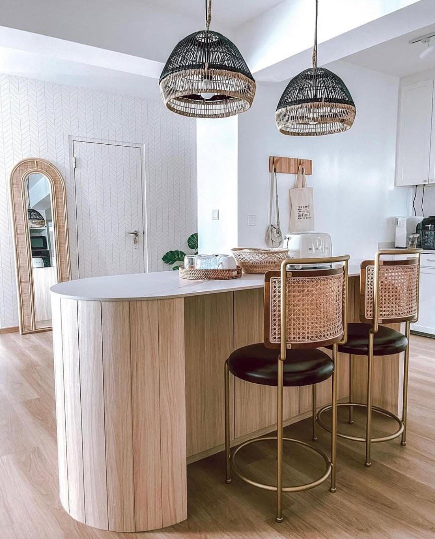 White herringbone pattern wallpaper covering a bomb shelter door and the wall around it in an open kitchen, with a curved timber island and rattan bar stools